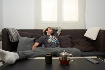 
Sleeping man in the living room of a house. He is sitting in a dark armchair and in front is a table with a kettle and a glass.