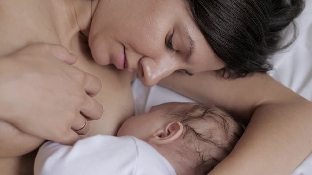 Young Woman Feeds Breast Milk To Her Newborn Baby Close Up While Lying In Bed