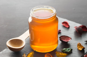 Honey jar without lid on black background with wooden spoon and dried flowers on black slate - Honey still life photo