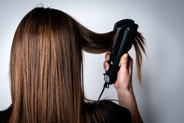 Young woman straightens her hair on gray background.