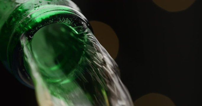 Stream of beer runs through the open green glass bottle in macro slow motion video, cold beer pours out, liquid flows, beverage tabletop, alcohol drink, 4k 120p Prores HQ 10 bit