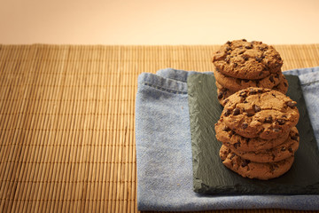 
Chocolate chip cookies on a wooden background with a gray cloth and a black plate.