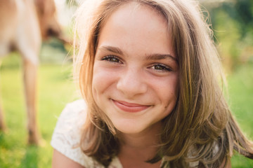 Naklejka premium Young teenager girl in a white dress laying in grass in summer sun and smiling into the lens.
