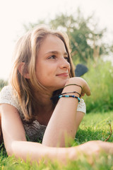 Young teenager girl in a white dress laying in grass in summer sun.