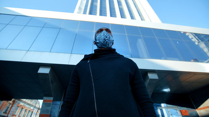 African American man out and about in the city streets during the day, wearing a face mask against air pollution and covid19 coronavirus, using his smartphone.