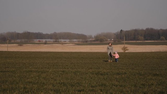 young mother with a child walk by hand from afar across the field