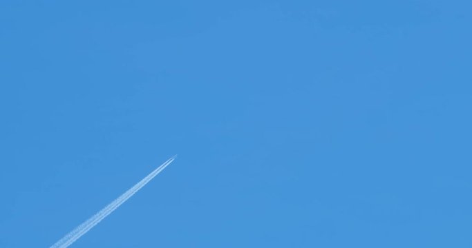Passenger plane flying at high altitude leaves a long white turbojet trail on a blue cloudless sky.