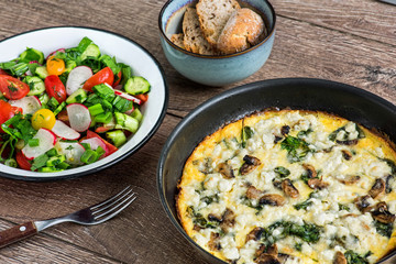 Homemade omlette with cheese, 
mushrooms and spinach in pan on wooden table. Homemade Frittata.