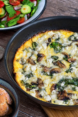 Homemade omlette with cheese, 
mushrooms and spinach in pan on wooden table. Homemade Frittata.