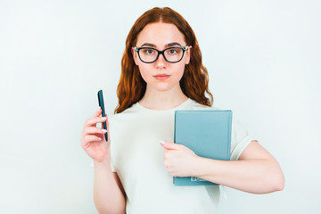 redheaded serious woman in eyeglasses holding pen in one hand and planner in another standing on...