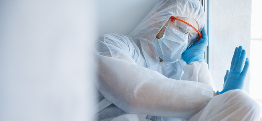 Loneliness quarantine, man in medical mask looks out window self isolation. Coronavirus pandemic concept