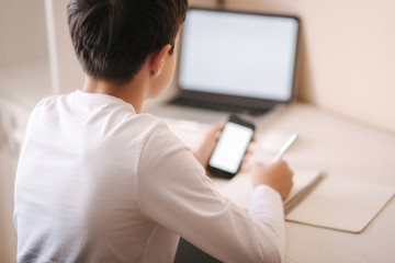 Schoolboy study at desk in his room. Boy use laptop and smartphone to writing in notebook. Books and tablet on the table. Study home during qurantine