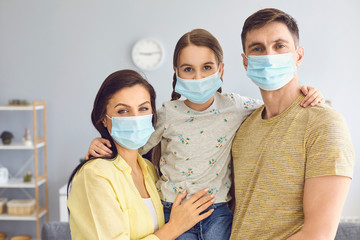 Family in medical masks on the face looks at the camera while standing in the room at home.