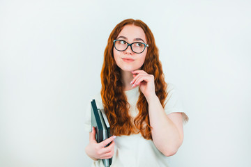 redheaded woman student in eyeglasses with books in her hand looks thoughtful standing on isolated white backgroung, learning and teaching concept