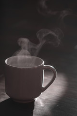 Silhouette of a hot drink mug with steam on a black background with empty place for text - vertical shot