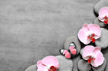 Spa stones and pink orchid on grey background and butterfly.