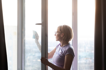 the young woman in glasses is concentrated and carefully washes a white plastic dirty glass window with a sponge in the apartment