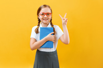 Portrait of a little schoolgirl with glasses on a yellow background. The child holds a book in his...