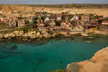 Panoramic skyline view of the famous Popeye Village at Anchor Bay at sunset with traditional Luzzu boats, beautiful colorful clouds and sky
