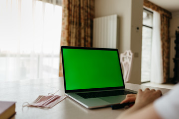 Coronavirus. A medical mask lies near a laptop in the Coronavirus. Medical mask lies near laptop in workplace. Green screen on laptopworkplace.