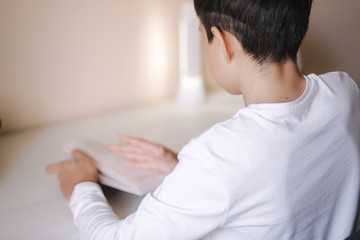 Young boy sitting at desk and read the book. Study at home during quarantine