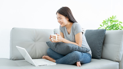 Asian woman relax resting with coffee cup sitting in sofa using laptop computer for watch movies streaming or happy working with smile