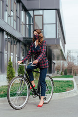Fototapeta na wymiar businesswoman in plaid mask riding bicycle near building