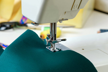 Sewing machine on the table, green cloth in the foreground. Close-up. Concept - sewing as a hobby.