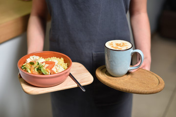 A plate with lunch and vegetables and a large mug of coffee in the hands of a waitress.