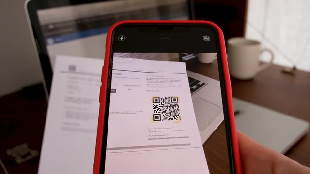 Hand with phone scans QR Code on background of a laptop with a workplace