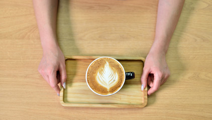 Female barista hands and a large cup of coffee with a pattern on the surface.