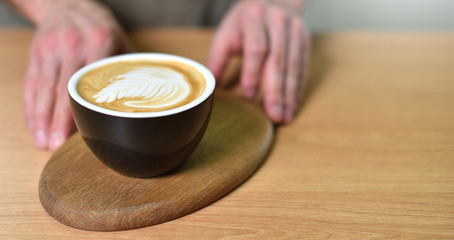 Male barista hands and a large cup of coffee with a pattern on the surface.