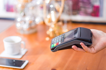 Cashier holding pos terminal in cafe and handing it over to customer. Cashless payment, pay by phone or with credit card. Cropped view