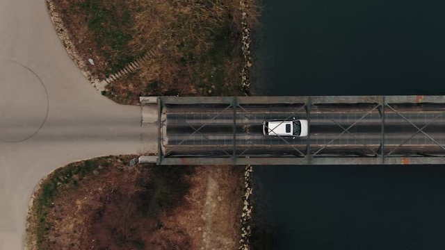 Aerial Drone Shot following a Car over a Bridge by a River vertically symetric with some Trees and some approaching Traffic in Switzerland countryside