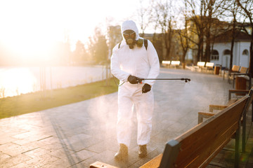 Man wearing protective suit disinfecting public places in the sun with spray chemicals to preventing the spread of coronavirus, pandemic in quarantine city. Covid -19. Cleaning concept.
