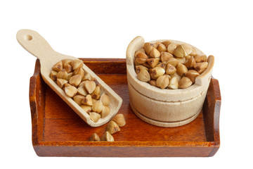 buckwheat in a wooden bowl and scoop on a tray isolated on white