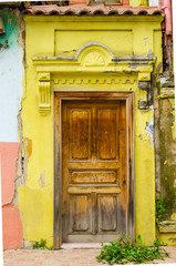 Element of  old abandoned non-residential building. nonsense door with peeling white paint. Porch, ruined steps, broken red railing. Windows with red bars. Yellow stucco on walls. Selective focus.