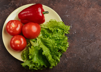 fresh veggies pepper tomatoes and lettuce on a plate on a brown background isolated