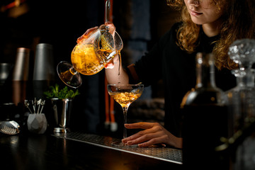 Close-up. Young pretty barman pours ready-made cocktail into glass.