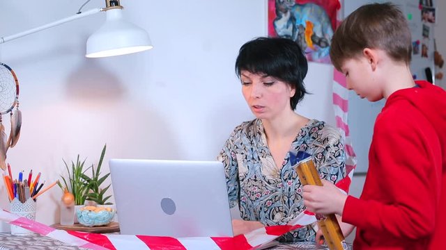 Home office, COVID 19. Home office in an apartment in self-isolation. Mom works on the computer. Son opens the pasta. Adaptation of people to self-isolation.