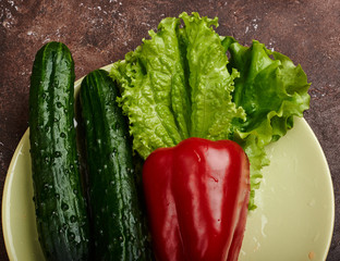 fresh veggies pepper  cucumbers and lettuce on a plate on a brown background isolated