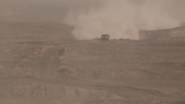 A military vehicle moves across the desert plain, the dust rises.