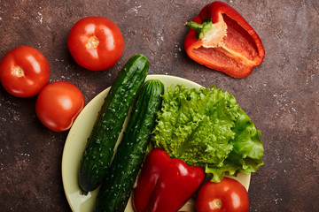 fresh veggies pepper tomatoes cucumbers and lettuce on a plate on a brown background isolated