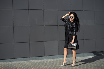 Total black fashion look. Happy attractive model with charming smile in fashionable sunglasses wearing stylish elegant dress and black fringed leather jacket. Model in trendy outfit.