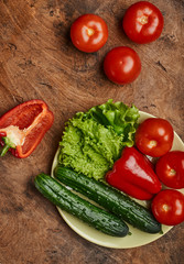 fresh veggies pepper tomatoes cucumbers and lettuce on a plate on a wooden background isolated