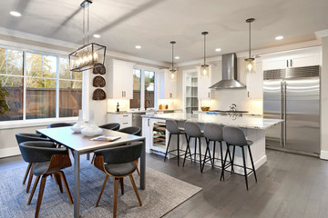 Large bright luxury kitchen interior with large dining room table and island with white marble.