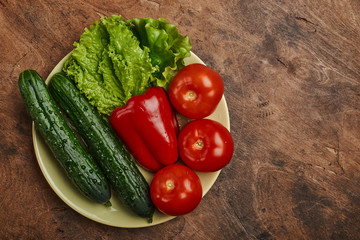 fresh veggies pepper tomatoes cucumbers and lettuce on a plate on a wooden background isolated