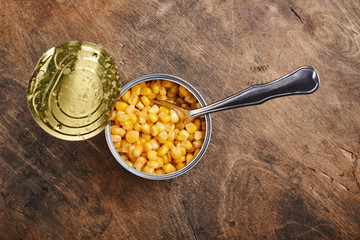 sweet corn grains witn spoon in a tin open can on a wooden background
