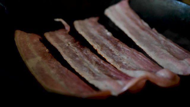 Streaky Bacon frying in black cast iron skillet