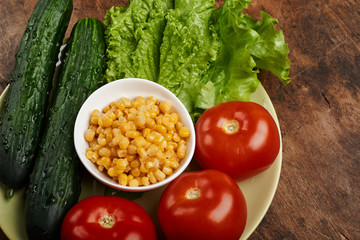 fresh veggies corn tomatoes cucumbers and lettuce on a plate on a wooden background isolated